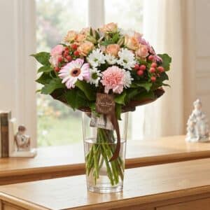 Bouquet de fleurs variées composé de roses pêche, de marguerites blanches, d'œillets roses et de baies rouges dans un vase en verre, par votre fleuriste à Boulogne-sur-Mer